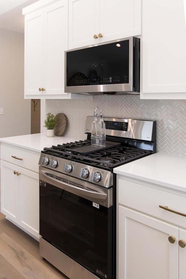 kitchen featuring tasteful backsplash, stainless steel appliances, light hardwood / wood-style floors, and white cabinets