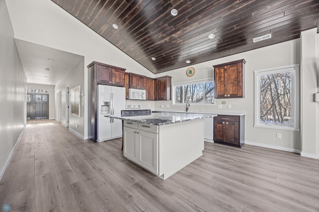 kitchen featuring refrigerator with ice dispenser, wood ceiling, a center island, light hardwood / wood-style floors, and dark stone counters