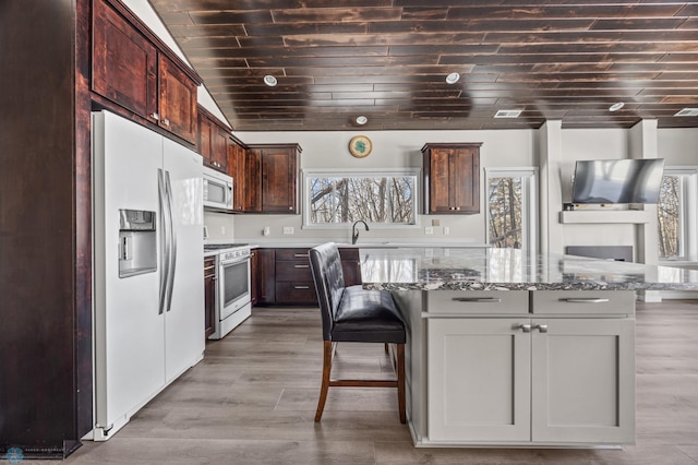 kitchen featuring a kitchen island, white gas range, refrigerator with ice dispenser, a kitchen bar, and light stone counters