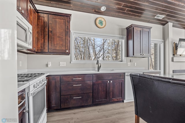 kitchen with dark brown cabinetry, sink, white appliances, and light wood-type flooring