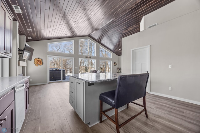 kitchen with a kitchen bar, a center island, light stone counters, wood ceiling, and light hardwood / wood-style flooring