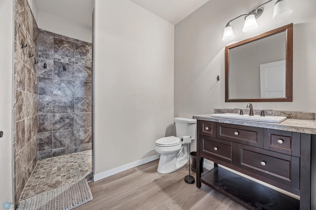 bathroom featuring hardwood / wood-style flooring, vanity, a tile shower, and toilet