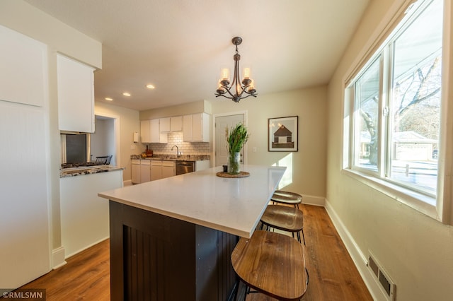 kitchen with white cabinetry, hanging light fixtures, dark hardwood / wood-style floors, dishwasher, and decorative backsplash