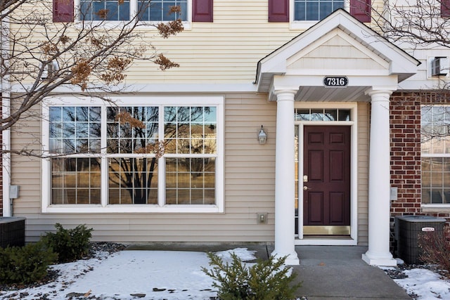 snow covered property entrance with cooling unit