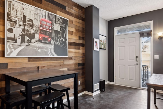 entrance foyer with dark wood-type flooring, a textured ceiling, and wooden walls