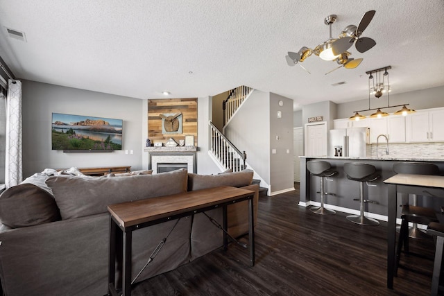 living room featuring sink, dark wood-type flooring, ceiling fan, a fireplace, and a textured ceiling