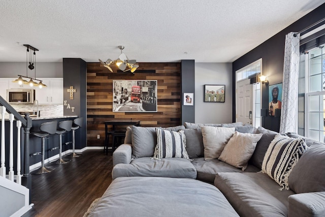 living room with a notable chandelier, wooden walls, dark hardwood / wood-style floors, and a textured ceiling