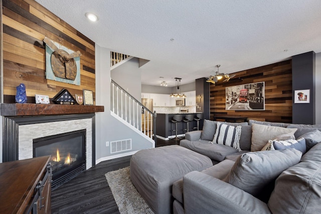 living room with a fireplace, dark hardwood / wood-style flooring, a textured ceiling, and wood walls