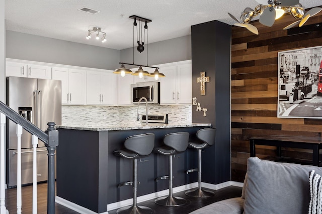 kitchen featuring a breakfast bar, white cabinetry, hanging light fixtures, appliances with stainless steel finishes, and light stone countertops