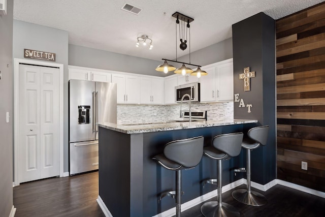 kitchen featuring a breakfast bar area, stainless steel appliances, light stone counters, white cabinets, and decorative light fixtures