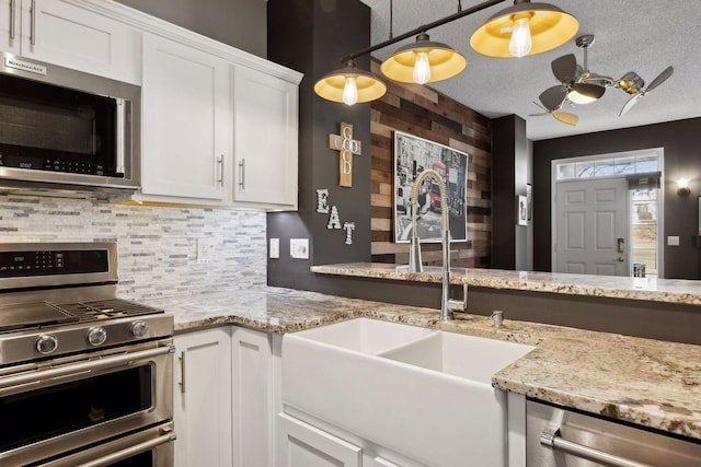 kitchen with white cabinetry, sink, hanging light fixtures, stainless steel appliances, and light stone countertops