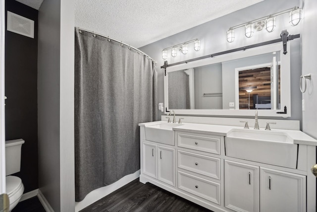 bathroom featuring hardwood / wood-style flooring, vanity, a textured ceiling, toilet, and walk in shower