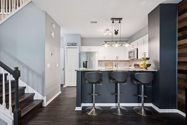 7316 Bunker Lake Blvd NW, Ramsey, MN 55303 - kitchen with stainless steel appliances, a peninsula, light stone counters, dark wood-style flooring, and a textured ceiling