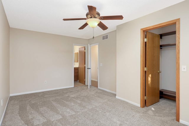 unfurnished bedroom featuring a walk in closet, light colored carpet, a closet, and ceiling fan