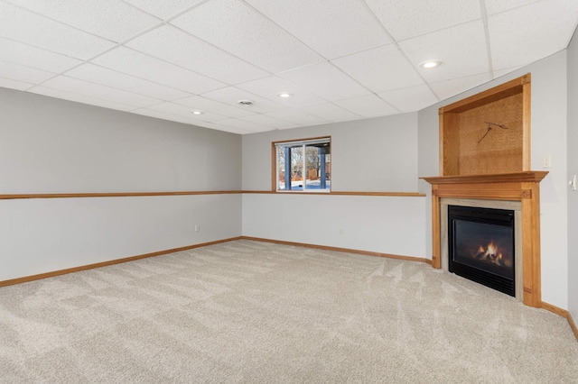 unfurnished living room with a large fireplace, carpet, and a drop ceiling