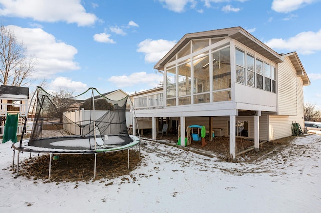 snow covered back of property featuring a sunroom, a playground, and a trampoline