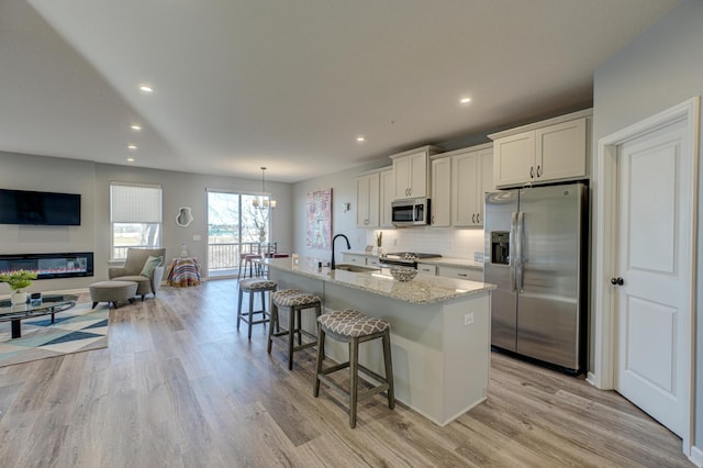 kitchen with appliances with stainless steel finishes, a breakfast bar, white cabinetry, an island with sink, and light stone counters