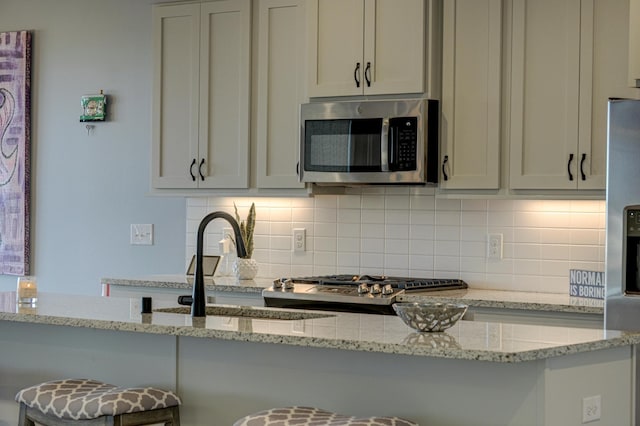 kitchen featuring stainless steel appliances, kitchen peninsula, light stone counters, and decorative backsplash