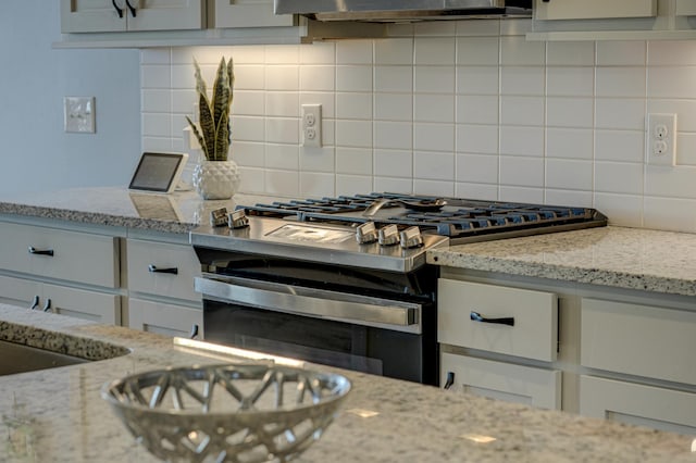 kitchen featuring light stone countertops, stainless steel gas range, and decorative backsplash