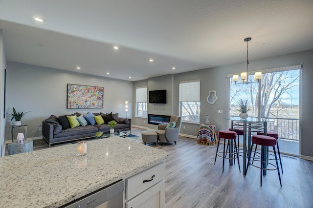 kitchen with pendant lighting, white cabinets, stainless steel dishwasher, light hardwood / wood-style floors, and light stone countertops