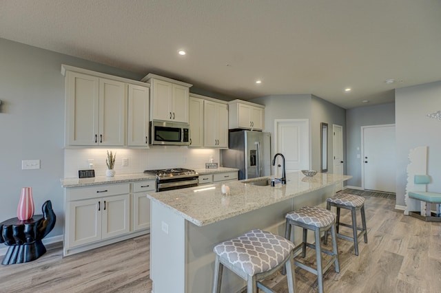 kitchen with appliances with stainless steel finishes, a kitchen island with sink, a breakfast bar area, and white cabinets