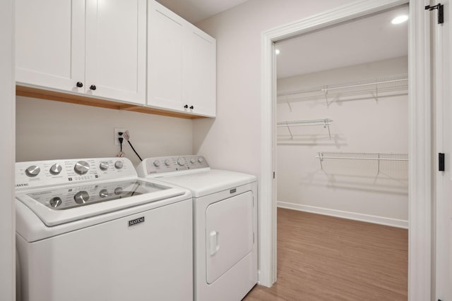 clothes washing area featuring cabinets, washing machine and dryer, and light wood-type flooring