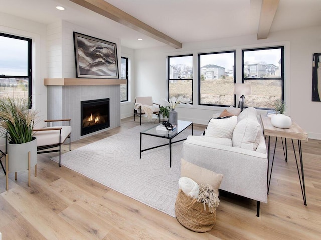 living room featuring beamed ceiling, a large fireplace, and light wood-type flooring