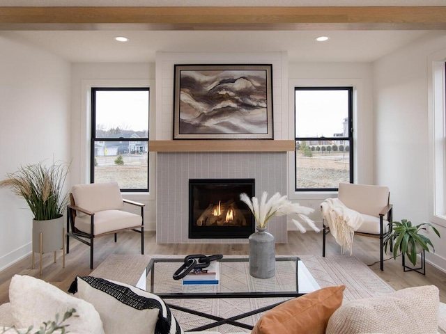 sitting room featuring light hardwood / wood-style flooring, a fireplace, beamed ceiling, and a healthy amount of sunlight