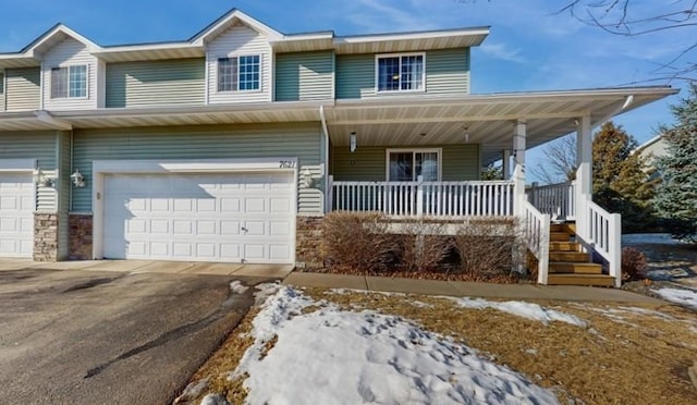 multi unit property featuring stone siding, a porch, driveway, and a garage