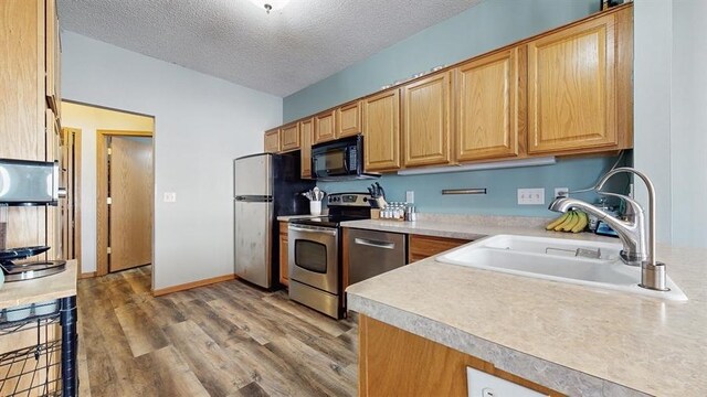 kitchen with a sink, a textured ceiling, wood finished floors, stainless steel appliances, and light countertops