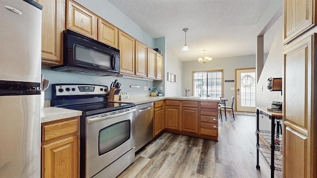 kitchen with light wood finished floors, appliances with stainless steel finishes, a peninsula, an inviting chandelier, and a sink