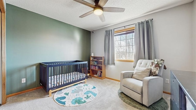 carpeted bedroom with baseboards, a textured ceiling, a crib, and a ceiling fan