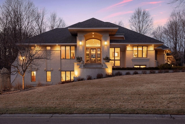 prairie-style house featuring a shingled roof, french doors, a front lawn, and stucco siding