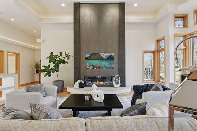 living room with recessed lighting, a high ceiling, a tiled fireplace, and wood finished floors