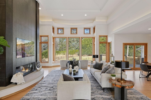 living area with recessed lighting, a large fireplace, a towering ceiling, and wood finished floors