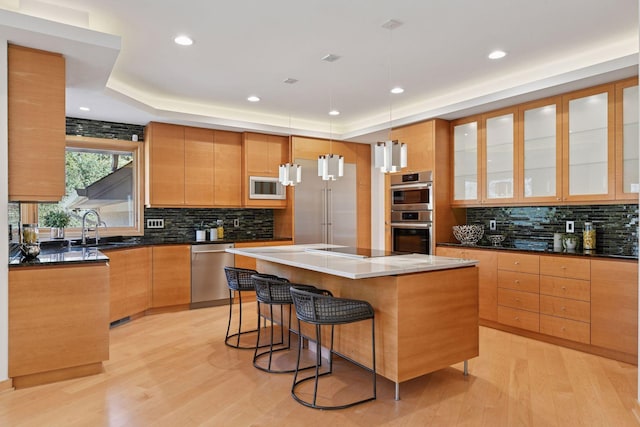 kitchen with a raised ceiling, light wood-style flooring, appliances with stainless steel finishes, a center island, and a kitchen bar