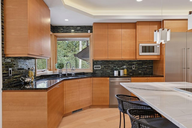 kitchen featuring light wood finished floors, dark stone counters, stainless steel appliances, and backsplash