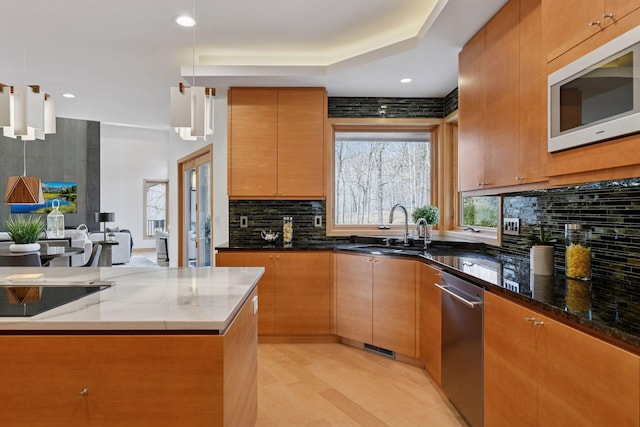 kitchen featuring white microwave, a sink, backsplash, dark stone counters, and decorative light fixtures