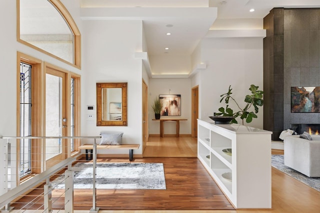 entryway featuring recessed lighting, a towering ceiling, a tiled fireplace, and wood finished floors