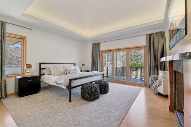 bedroom with a fireplace, wood finished floors, access to outside, french doors, and a tray ceiling