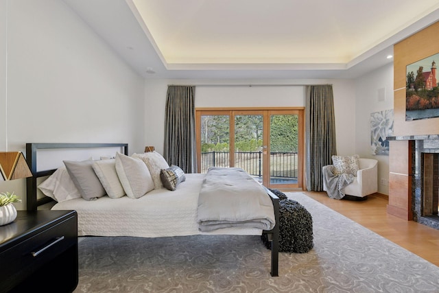 bedroom featuring a tray ceiling, wood finished floors, a fireplace with flush hearth, and access to exterior