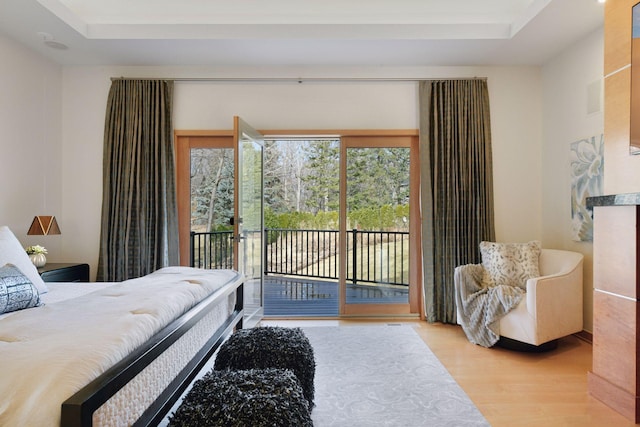 bedroom with access to outside, a tray ceiling, and wood finished floors