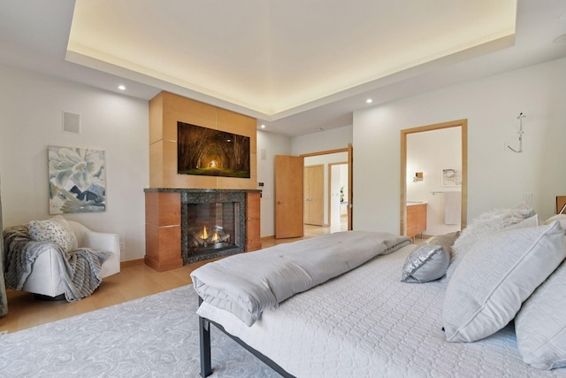 bedroom with a warm lit fireplace, a raised ceiling, recessed lighting, and wood finished floors