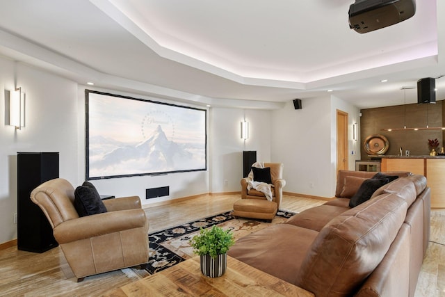 home theater with light wood-type flooring, a raised ceiling, visible vents, and baseboards