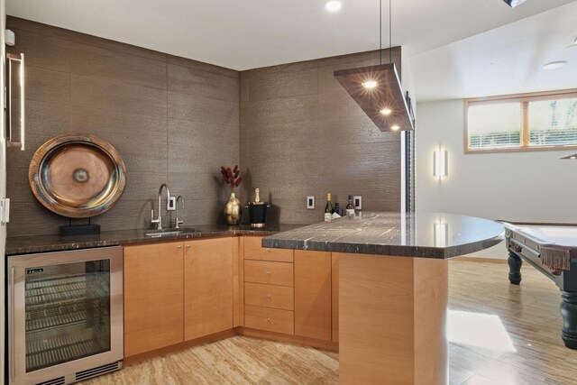 bar featuring beverage cooler, tasteful backsplash, decorative light fixtures, light wood-type flooring, and a sink