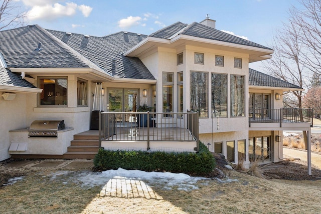 rear view of house featuring a deck, a chimney, an outdoor kitchen, and stucco siding