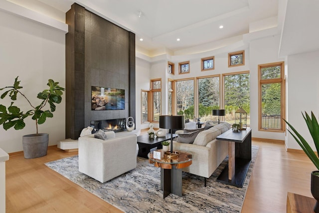 living room featuring recessed lighting, a tile fireplace, a high ceiling, and light wood-style floors