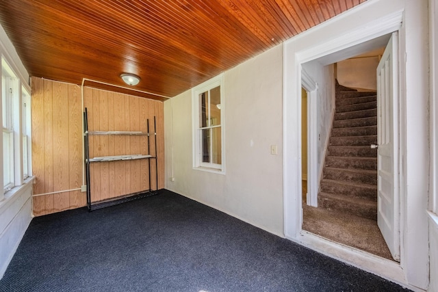 interior space featuring dark carpet, wooden walls, and wooden ceiling