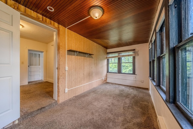 carpeted spare room featuring wood ceiling, wooden walls, and vaulted ceiling