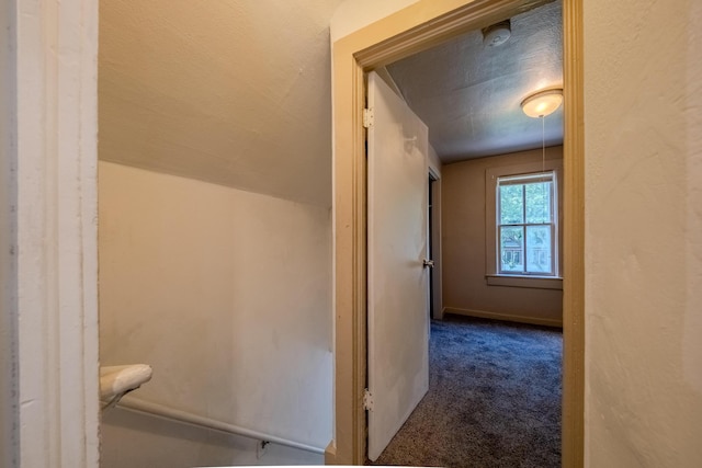 hall with lofted ceiling and dark carpet